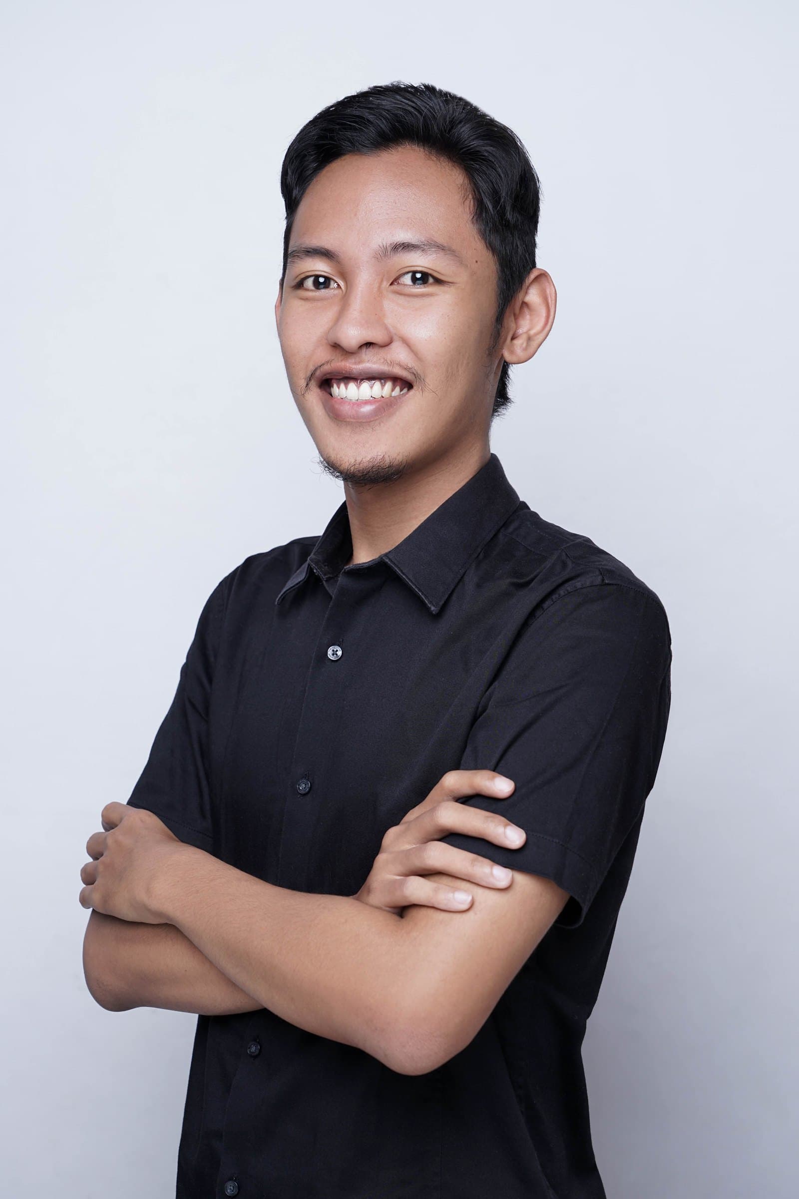 Portrait of Farid Zam, arms crossed, smiling, in a black shirt